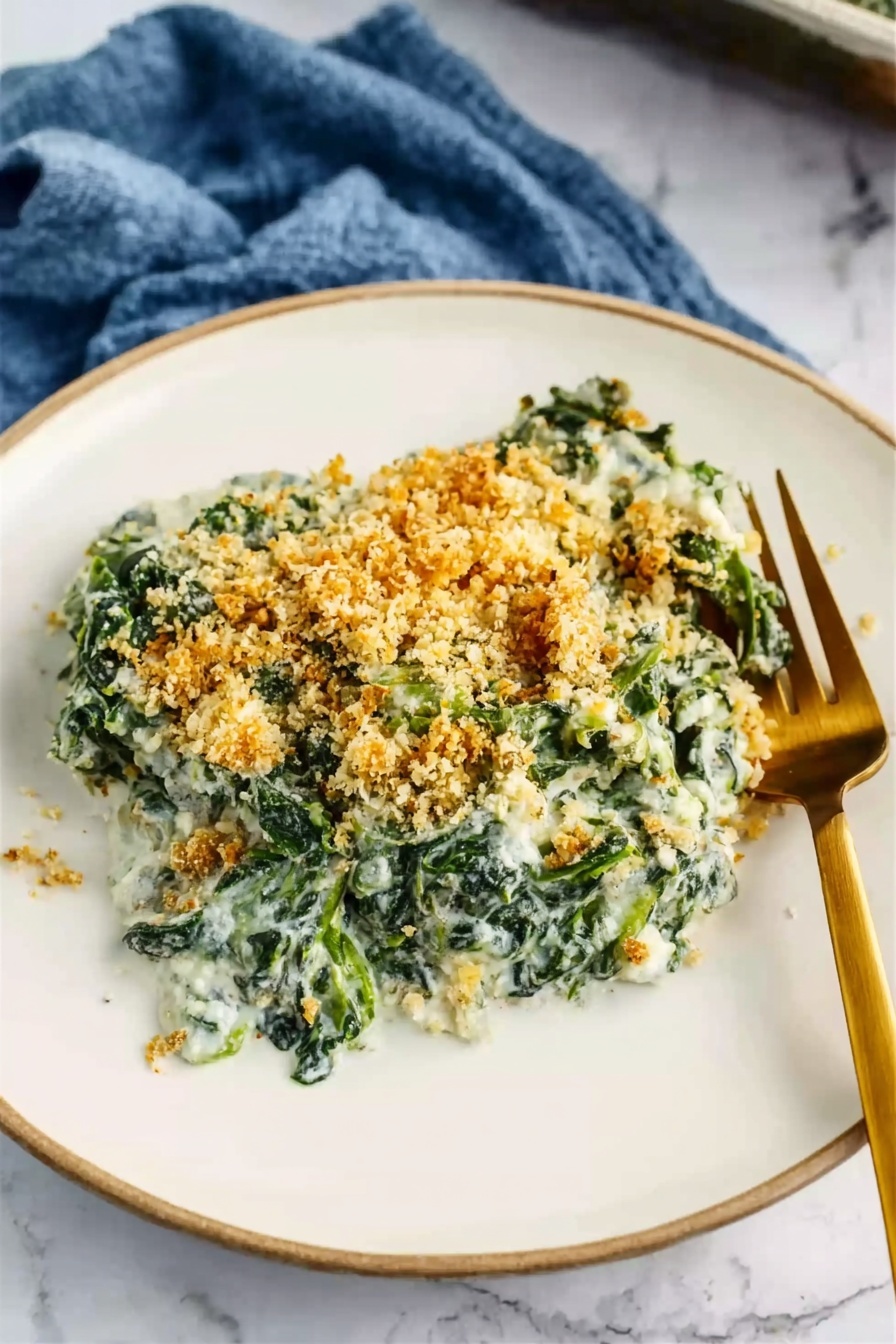 A white plate holds a serving of creamy spinach casserole topped with a golden, crumbly breadcrumb layer. The spinach mixture looks soft and green, mixed with a white creamy sauce. The golden crumbs are spread unevenly on top, adding a crunchy texture contrast to the smooth spinach below. A gold fork rests on the right side of the plate, its tines partly buried in the food. The plate sits on a white marbled surface, with a blue cloth casually placed in the background. Photo taken with an iphone --ar 2:3 --v 7 - Creamed Spinach Gratin, cheesy creamed spinach side dish, crispy breadcrumb spinach casserole, easy creamed spinach recipe, holiday side dishes