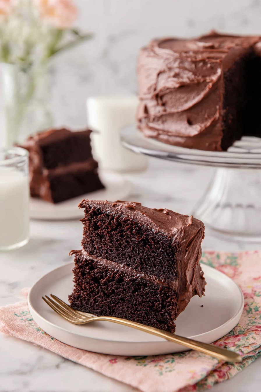 A slice of two-layer chocolate cake with dark, rich cake layers and thick, smooth chocolate frosting both between the layers and on top, presented on a white plate. The frosting on top has a slightly textured, creamy finish with gentle swirls. In the background, there is a full chocolate cake with the same thick frosting on a clear glass cake stand, and another slice of cake on a white plate. Next to the front plate is a glass of milk and a gold spoon resting on a fabric napkin with a soft floral pattern, all set on a white marbled surface. photo taken with an iphone --ar 2:3 --v 7 - Ultimate Chocolate Cake, moist chocolate cake, rich chocolate dessert, homemade chocolate cake, easy chocolate cake recipe