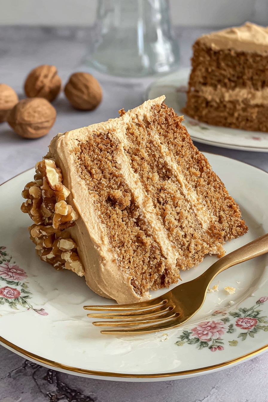 A two-layer round cake with light brown frosting between and on top of the layers. The top layer of frosting is decorated with a ring of chopped walnuts around the edge. The cake is placed on a clear glass cake stand with a patterned surface. The background shows a white marbled texture surface with some whole walnuts scattered around and a pink cloth napkin on the side. Photo taken with an iphone --ar 2:3 --v 7 - Coffee Walnut Cake with Fluffy Frosting, walnut coffee cake, easy coffee cake recipe, moist walnut cake, fluffy frosting cake